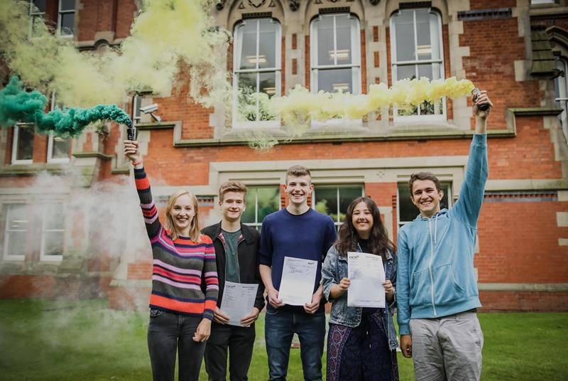 cheadle hulme school's upper sixth form students and class of 2017 are all smiles as they hold colourful flares and their results on their A Level exam results day 