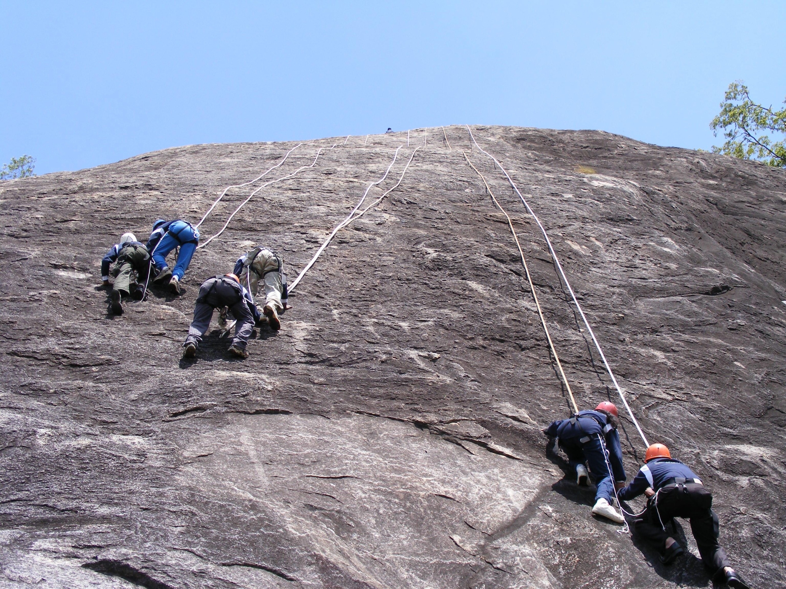 climbers scale a mountain rock face in climbing gear and red hats during an Outward Bound activity summer camp