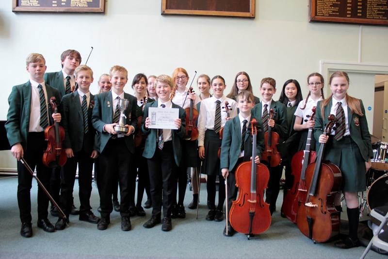 music students in cheadle hulme school's orchestra hold string instruments including violins violas cellos and double bass and their trophy cup after winning first prize in the Adderley edge music festival competition 